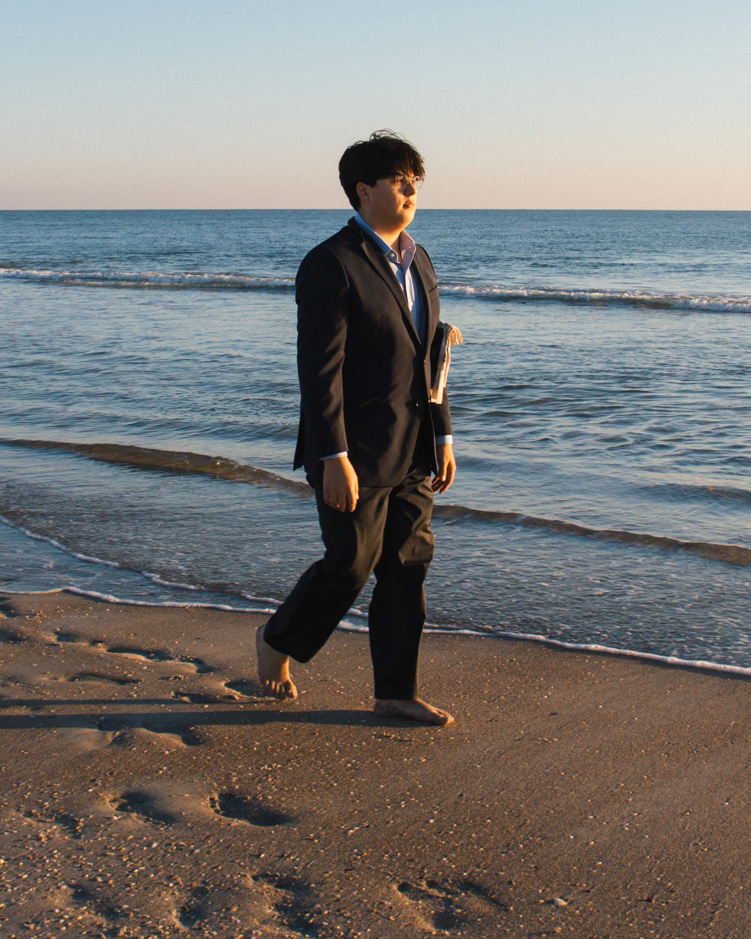 Miguel Javiel in a dark suit walking along the shoreline at sunrise
